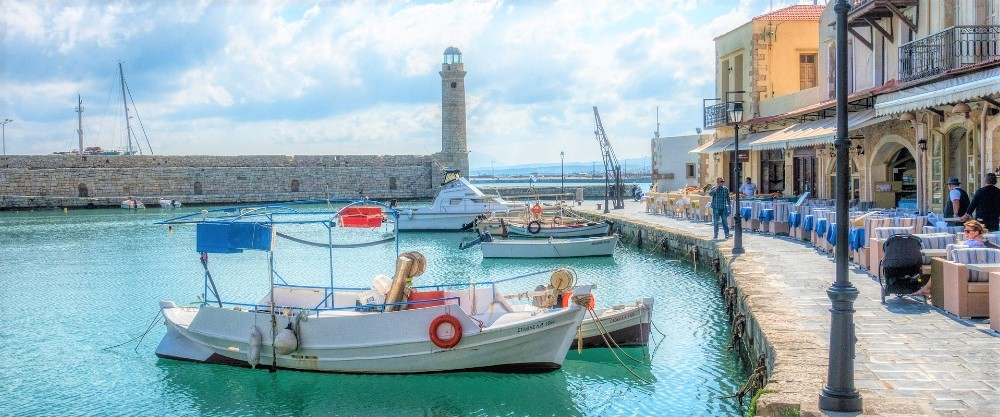 Rethymno's seafront promenade with traditional fishing boats moored in the harbour and colourful buildings facing the sea.